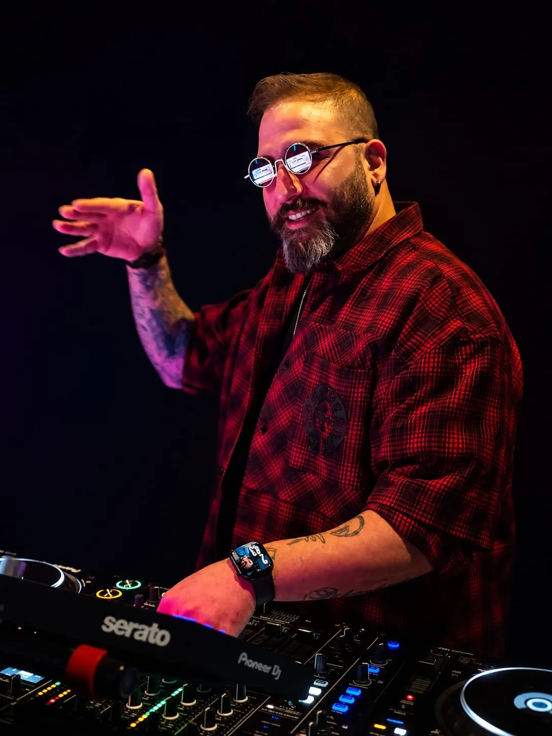 Bearded DJ in round sunglasses waving over a Serato mixer