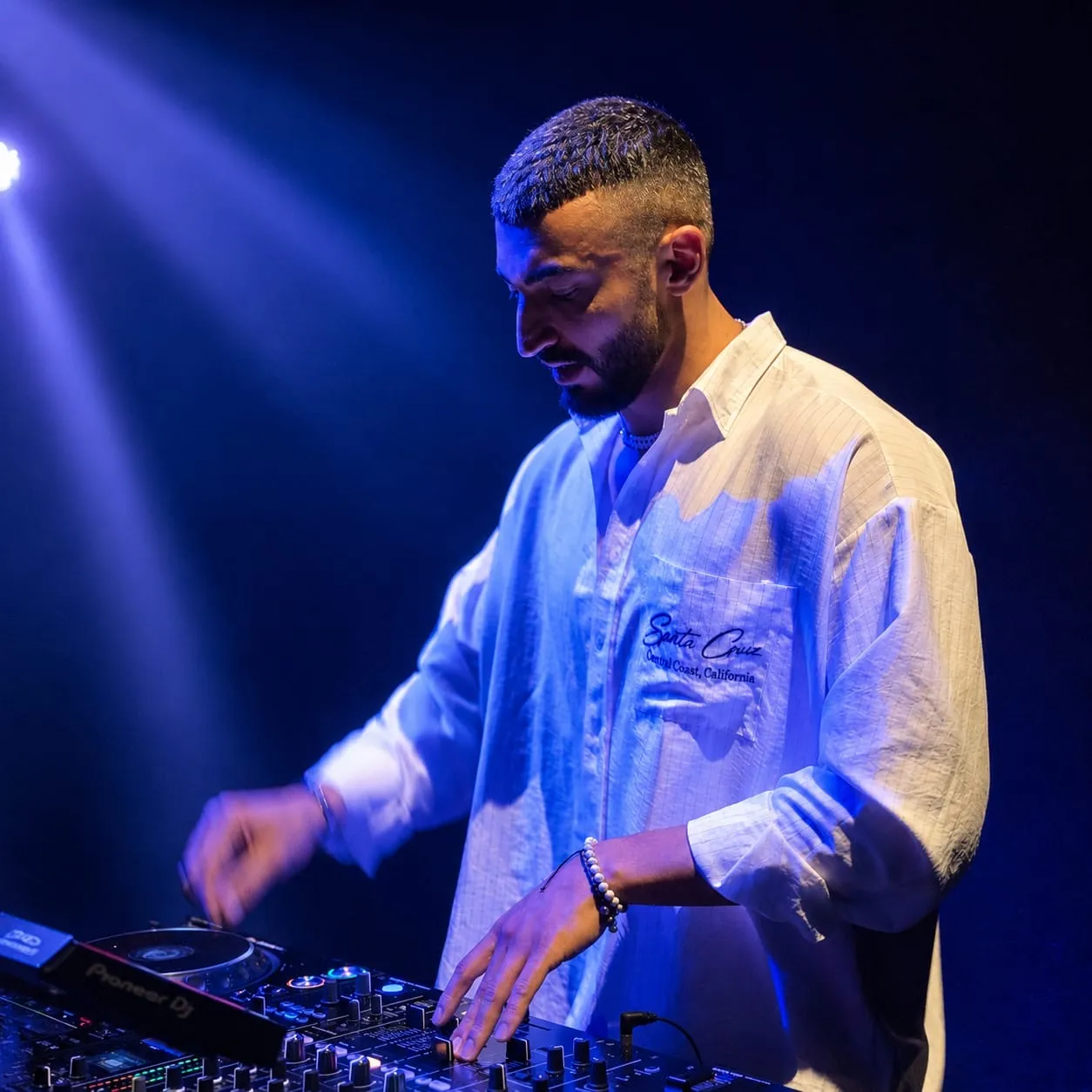 DJ in a white shirt leaning over the mixer in a cool blue spotlight