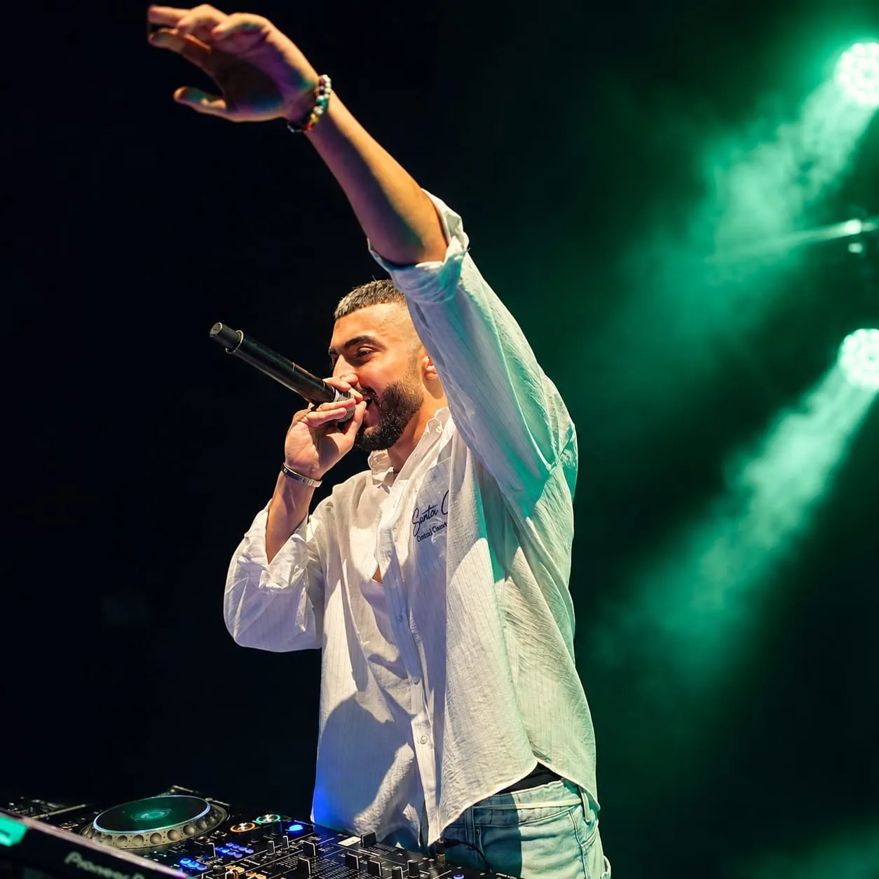 Singer in a white shirt with a microphone and one arm raised under green light