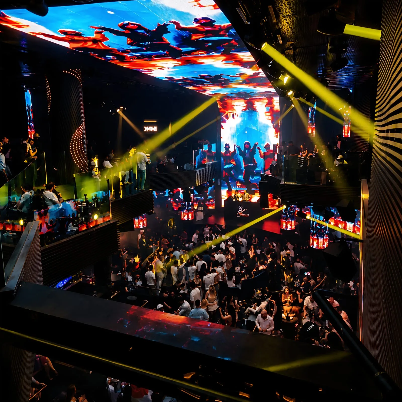 View from the upper deck over the main room, with a giant LED screen and yellow beams above the crowd